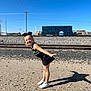 child, girl, outdoor, sporty, cheerleader, shadow, gravel, train_tracks, blue_sky, sunny, playful, smiling, white_shoes, black_skirt, hair_bow, daylight, posing, young, fun, casual