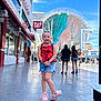 Abriella joined the competition — help win amazing prizes! child, girl, smiling, red_top, denim_shorts, pink_shoes, urban, sidewalk, street, daylight, people, backpack, blue_sky, architecture, signage, casual_clothing, outdoor, portrait, tourist, cityscape