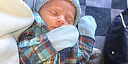 Luke joined the competition — help win amazing prizes! baby, newborn, sleeping, plaid_shirt, knit_hat, mittens, pacifier_clip, hand, person, indoor, floor, checkered_floor, clothing, cozy, resting, infant, cute, child, portrait, closeup