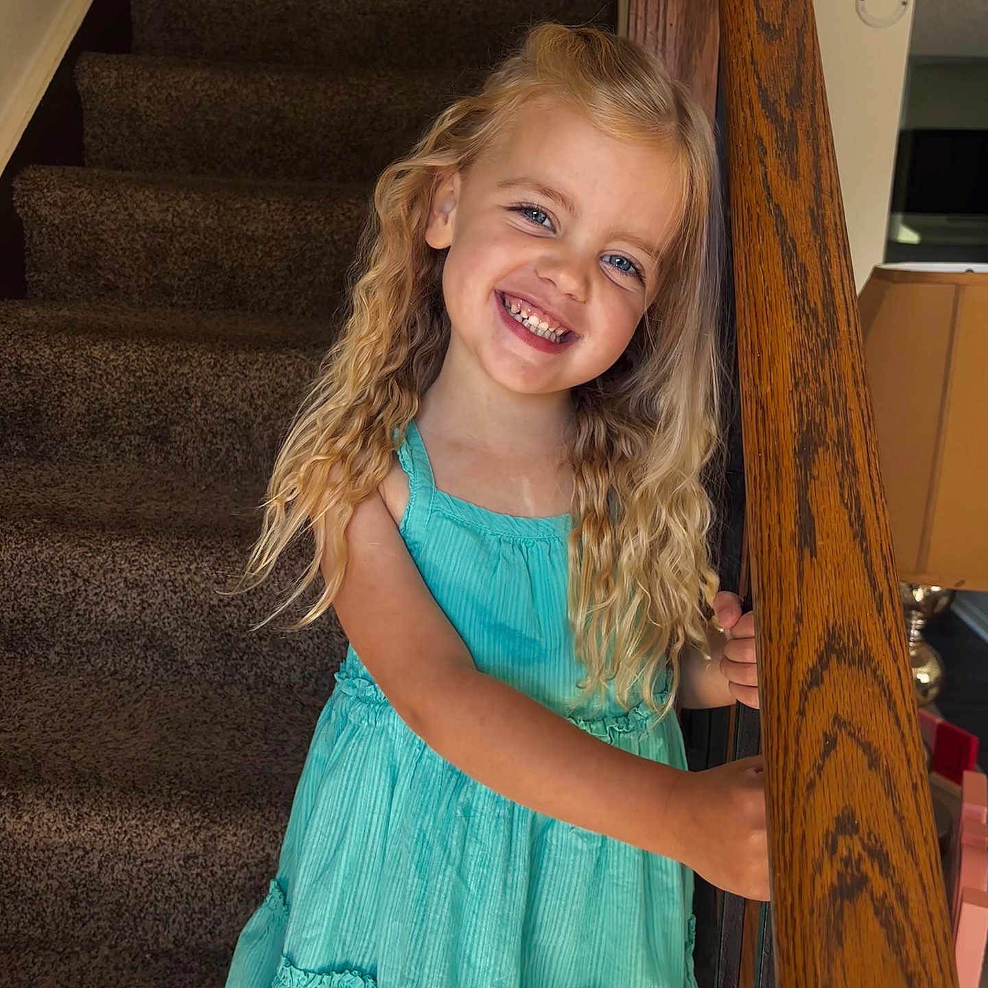 Elsie joined the competition — help win amazing prizes! child, girl, smiling, blonde_hair, curly_hair, dress, blue_dress, stairs, carpet, wooden_railing, indoor, home, railing, person, happy, portrait, standing, young, cute, smile