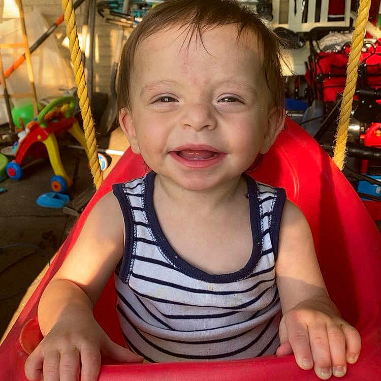 Zachariah joined the competition — help win amazing prizes! casual, child, cute, daylight, face, fun, garage, hands, happy, outdoor, person, plastic, play, red, smiling, striped_shirt, sunlight, swing, toddler, toy