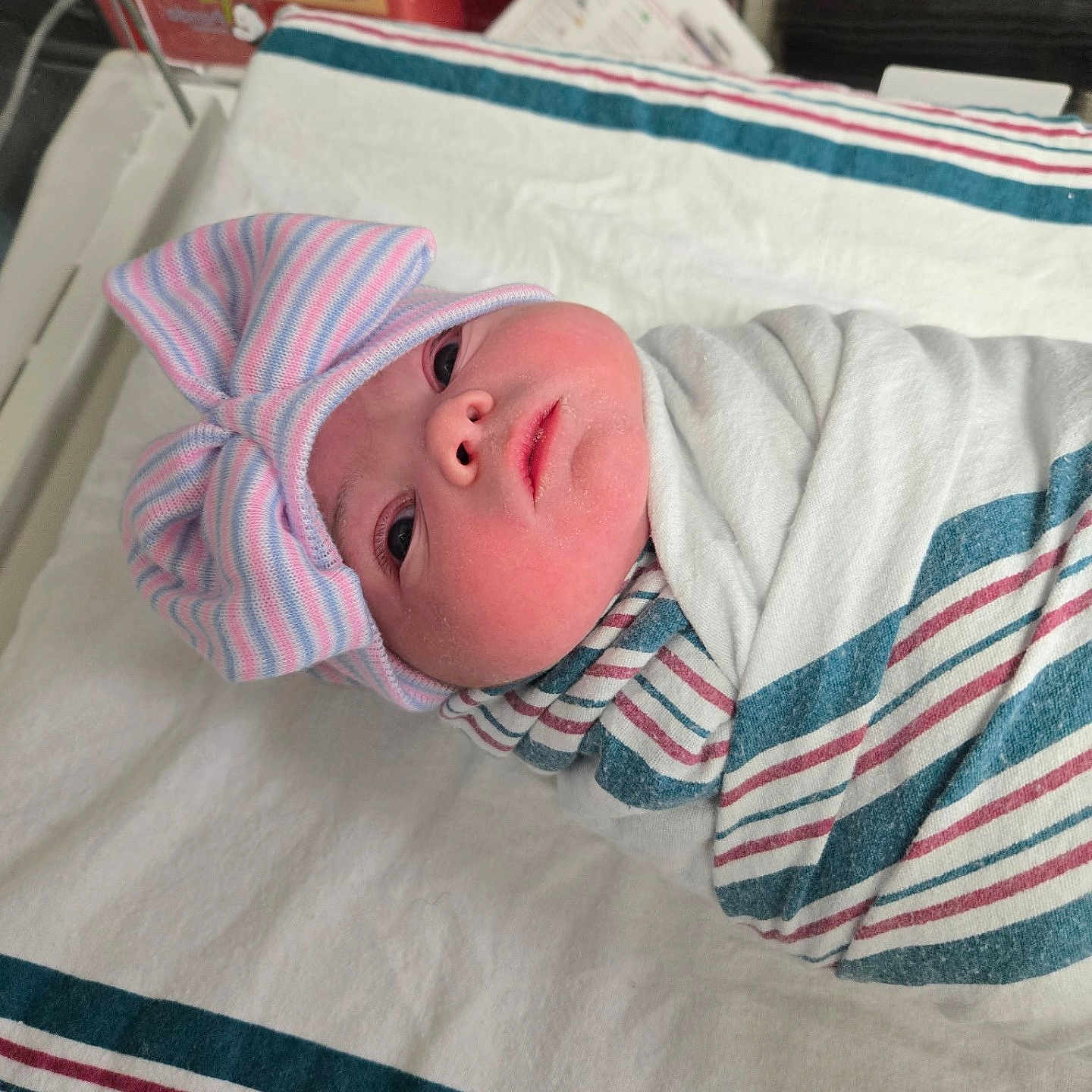 Selina is registered to the contest to win money with this photo: newborn, baby, swaddled, hat, bow, striped_blanket, hospital, bassinet, medical_equipment, infant, cute, sleeping, person, face, bed, blanket, indoors, headwear, newborn_baby, baby_clothing