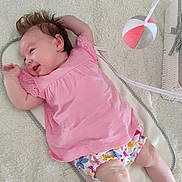 Jade participe au concours pour gagner de l'argent avec cette photo : baby, infant, crib, blanket, pink_clothing, floral_shorts, toy, soft_toy, hanging_toy, smiling, happy, lying_down, person, indoor, head, face, hand, foot, arm, hair