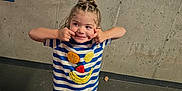 Ellie is registered to the contest to win money with this photo: child, kid, playful, parking_garage, concrete_wall, striped_shirt, shorts, fruit_patches, white_sandals, silly_face, cheeks, urban, outdoor, standing, expression, casual_clothing, hair_tied, daylight, person, smile