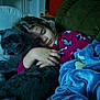 child, sleeping, cat, hugging, blanket, couch, indoor, cozy, relaxing, young, peaceful, home, furniture, comfort, pet, animal, person, resting, curly_hair, warm_lighting