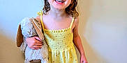 Ellie joined the competition — help win amazing prizes! child, girl, smiling, yellow_dress, hair_bow, plush_toy, bunny, barefoot, standing, indoor, floor, wall, happy, cute, portrait, young_child, toy, clothing, person, playful