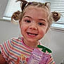 child, girl, smile, pigtails, striped_shirt, snack, indoor, window, blinds, nutrition_label, happy, portrait, holding, cute, young, person, face, hand, casual, daylight