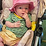 Freyja joined the competition — help win amazing prizes! baby, pink_hat, green_shirt, stroller, cushions, toy, hand, face, expression, curious, infant, clothing, soft, indoor, child, sitting, cute, small, playful, person