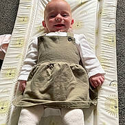 Freyja is registered to the contest to win money with this photo: baby, smiling, infant, changing_mat, lion_pattern, dress, white_tights, carpet, happy, child, cute, indoors, person, apparel, fabric, lying_down, small_child, portrait, clothing, soft_lighting