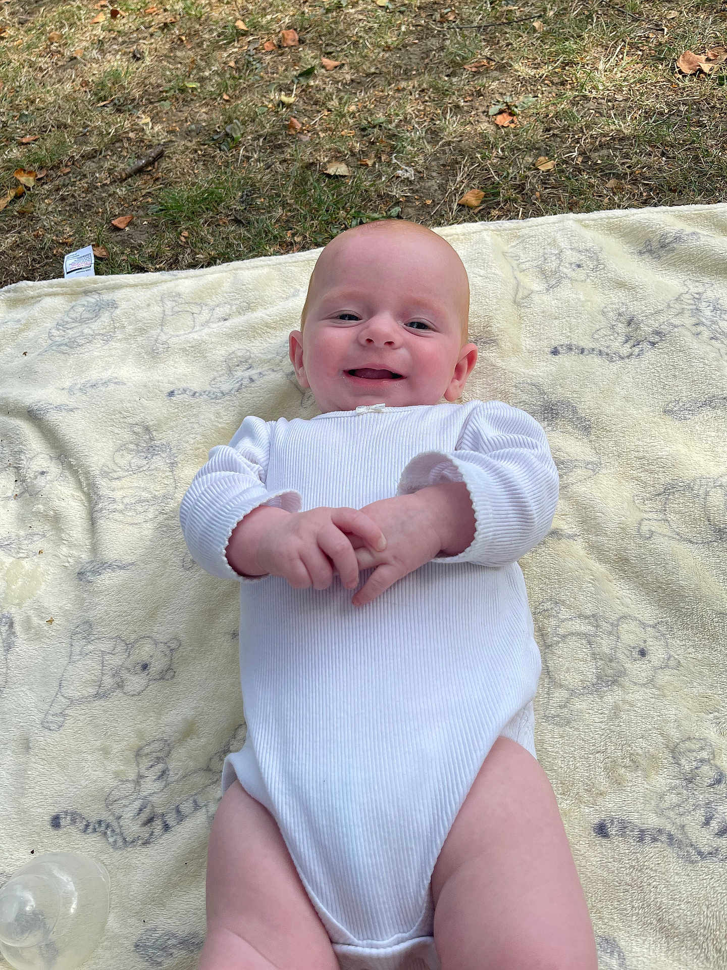 Freyja joined the competition — help win amazing prizes! baby, infant, smiling, white_onesie, blanket, outdoor, grass, fall_leaves, happy, person, child, cute, lying_down, young, face, skin, natural_light, casual, playful, baby_bottle