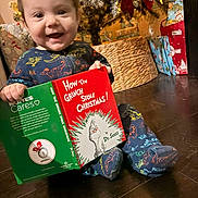 Braxton Jaxx joined the competition — help win amazing prizes! baby, child, christmas_tree, holiday, book, reading, dinosaur_pajamas, floor, gift_wrap, decorations, smiling, indoor, festive, toddler, present, cute, happy, christmas, cozy, seasonal