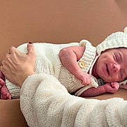 Theo joined the competition — help win amazing prizes! newborn, baby, smiling, knitted_clothing, white_outfit, bear_ears_hat, peaceful, sleeping, tiny_feet, adult_hand, cradling, soft_texture, brown_background, infant, cute, portrait, cozy, warm, close_up, human