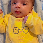 Theo Victor is registered to the contest to win money with this photo: baby, infant, newborn, onesie, yellow_clothing, cartoon_chick, glasses_graphic, blanket, towel, portrait, close_up, face, eyes, hand, bedding, cute, soft_texture, indoor, laying_down, infant_garment