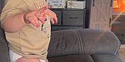 Braxton is registered to the contest to win money with this photo: toddler, child, smiling, pointing, couch, living_room, television, remote_control, wooden_table, furniture, indoors, person, diaper, casual_clothing, happy, face, hair, toy, cabinet, cozy