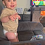 toddler, child, smiling, pointing, couch, living_room, television, remote_control, wooden_table, furniture, indoors, person, diaper, casual_clothing, happy, face, hair, toy, cabinet, cozy