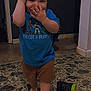 toddler, child, blue_tshirt, toy_story, cap, barefoot, floor, sippy_cup, indoor, playful, walking, hand_on_face, smiling, shorts, person, young_child, home, tile_floor, cup, casual_clothing