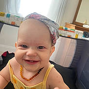 Ottline joined the competition — help win amazing prizes! baby, smiling, headscarf, necklace, playpen, indoor, child, happy, cute, person, infant, yellow_clothing, reaching, portrait, face, cheerful, bright, daylight, home, baby_girl