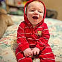 baby, child, red_hoodie, striped_clothing, smiling, sitting, bedspread, floral_pattern, indoors, cute, toddler, happy, portrait, hand_holding, infant, cozy, hooded, casual_wear, person, young_child