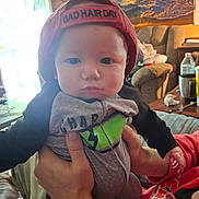 Gabriel joined the competition — help win amazing prizes! baby, child, cap, hat, tattoo, hands, living_room, couch, painting, furniture, person, indoor, clothing, expressionless, infant, holding, adult, casual, portrait, cute