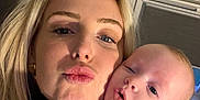 Elisa a rejoint le concours — aidez-le/la à gagner de superbes lots ! woman, baby, close_up, selfie, indoor, portrait, face, puckered_lips, curious, light_skin, blonde_hair, baby_clothing, floral_pattern, cozy, warm_light, expression, holding, family, child, parent