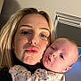 woman, baby, close_up, selfie, indoor, portrait, face, puckered_lips, curious, light_skin, blonde_hair, baby_clothing, floral_pattern, cozy, warm_light, expression, holding, family, child, parent