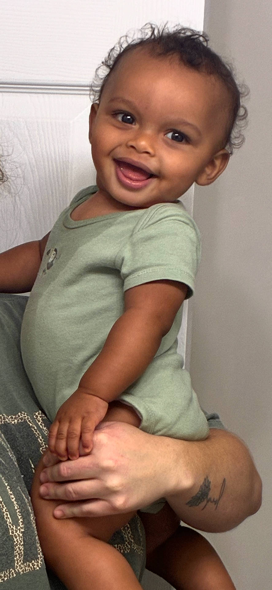 Aqeil joined the competition — help win amazing prizes! arm, baby, child, curly_hair, cute, door, expression, face, green_onesie, hand, happy, holding, indoor, people, person, portrait, skin, smiling, tattoo, toddler