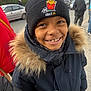 child, smiling, winter_coat, fur_hood, beanie, outdoor, cold_weather, street, car, person, happy, face, clothing, headwear, urban, people, daytime, casual, jacket, portrait