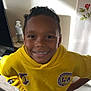 child, boy, smiling, yellow_hoodie, lakers_logo, indoor, hand_sanitizer, rose_decal, wall, casual_clothing, short_hair, standing, happy, portrait, person, black_pants, white_shoes, home, confident, young