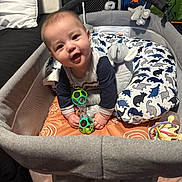 Brian Ortiz Jr. is registered to the contest to win money with this photo: baby, smiling, playpen, toy, rattle, cushion, dinosaur_pattern, pillow, infant, child, indoor, happy, cute, soft_toys, baby_clothes, person, face, seated, playtime, nursery