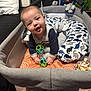 baby, smiling, playpen, toy, rattle, cushion, dinosaur_pattern, pillow, infant, child, indoor, happy, cute, soft_toys, baby_clothes, person, face, seated, playtime, nursery