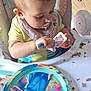 bib, cartoon_character, child, cute, eating, face, feeding, food, high_chair, indoor, mealtime, messy, peas, person, pink_food_bits, plate, spoon, table, toddler, yogurt
