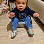 basin, blue_pants, books, bookshelf, child, colorful_socks, curly_hair, expression, face, floor, furniture, hand, home, indoor, room, sitting, sweater, toddler, toy, wood_floor