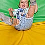 active, baby, cartoon_print, child, cute, denim_shorts, green_background, happy, indoor, joyful, legs, padded_surface, person, playful, smiling, socks, toddler, tshirt, yellow_background, young_child