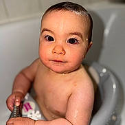 Emmy is registered to the contest to win money with this photo: baby, child, bath, water, wet_skin, bath_seat, holding, metal_bar, closeup, face, eyes, skin, infant, cute, indoors, toddler, expression, portrait, human, sitting