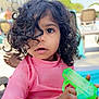 child, toddler, curly_hair, pink_clothing, water_gun, outdoor, sunny, poolside, lounge_chair, expression, portrait, hand, summer, playful, toy, young, casual, daylight, skin, person