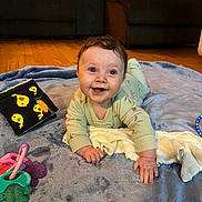 Paisley is registered to the contest to win money with this photo: baby, infant, tummy_time, smile, blanket, soft_book, toy, teether, pajamas, towel, drool, hands, face, eyes, living_room, couch, hardwood_floor, playmat, indoor, happy