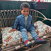 Hector participe au concours pour gagner de l'argent avec cette photo : bench, boy, casual_clothing, child, cushion, daylight, denim_jacket, fence, floral_pattern, happy, house, jeans, outdoor, plant_pot, portrait, roof, shoes, sitting, smile, socks