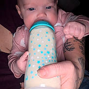 Madison is registered to the contest to win money with this photo: baby, bottle, feeding, infant, hand, tattoo, pink_clothing, blue_stars, milk, closeup, portrait, child, cute, human, skin, fingers, nourishment, drink, person, dark_background