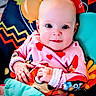 Madison is registered to the contest to win money with this photo: baby, infant, child, onesie, heart_pattern, colorful, cushion, pattern, face, hands, drool, sitting, playful, bright_colors, cartoon_characters, cute, portrait, indoors, childrens_clothing, young