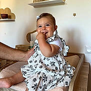 Saori participe au concours pour gagner de l'argent avec cette photo : baby, child, smiling, sitting, dress, white, black_flower_pattern, hand, changing_table, room, clock, shelf, decor, star, fingers_in_mouth, happy, infant, cute, indoor, person