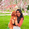 woman, dog, pet, smiling, outdoor, spring, flower, cherry_blossom, green_grass, tree, nature, portrait, happy, curly_fur, holding, leash, urban, casual_clothing, daylight, backyard