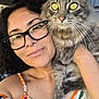 woman, cat, selfie, glasses, yellow_eyes, curly_hair, tabby_cat, close_up, colorful_clothing, portrait, smile, indoor, face, pet, holding, shoulder, whiskers, feline, casual, friendly