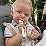 baby, blond_hair, child, closeup, curious, daylight, expression, face, feeding, greenery, high_chair, nature, outdoor, portrait, seat, seat_belt, spoon, toddler, trees, white_shirt