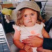 Nina a rejoint le concours — aidez-le/la à gagner de superbes lots ! toddler, child, person, hat, cap, indoor, cushion, table, hand, clothing, plant, wall, face, sitting, expression, furniture, curtain, nail_polish, diaper, portrait