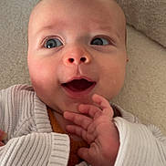 Nelson participe au concours pour gagner de l'argent avec cette photo : baby, infant, face, hand, sweater, knitwear, blanket, closeup, expression, cute, child, person, skin, blue_eyes, smile, lying_down, cozy, soft_texture, portrait, indoor