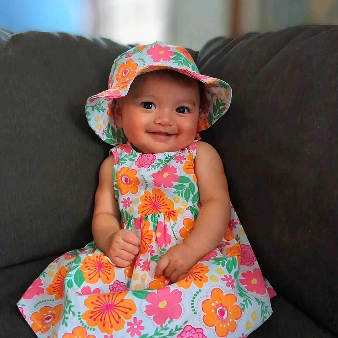 Kiana joined the competition — help win amazing prizes! baby, bonnet, cap, clothing, couch, cushion, dress, face, formalwear, furniture, happy, hat, head, homedecor, person, photography, portrait, sitting, smile, sunhat