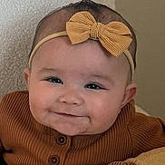 Nyla is registered to the contest to win money with this photo: baby, infant, headband, bow, smile, chubby_cheeks, portrait, indoor, pillow, blanket, brown_outfit, buttons, eyes, face, cute, soft_texture, wall, sitting, closeup, adorable