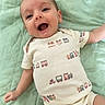 baby, infant, smiling, onesie, clothing, pattern, train, quilted_blanket, mint_green, happy, lying_down, cute, child, human, portrait, baby_girl, baby_boy, soft_texture, indoors, close_up