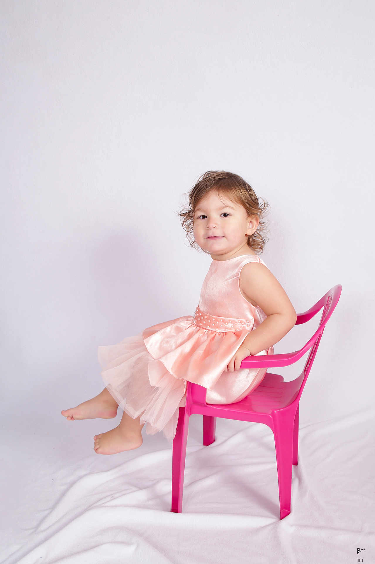 Mya participe au concours pour gagner de l'argent avec cette photo : toddler, child, pink_dress, plastic_chair, barefoot, studio, white_background, smiling, curly_hair, portrait, cute, sitting, playful, young_child, innocent, fashion, happy, girl, posing, indoor