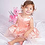 Mya a rejoint le concours — aidez-le/la à gagner de superbes lots ! toddler, child, dress, peach, pink_unicorn, plush_toy, soft_blanket, smile, curly_hair, indoor, portrait, cute, sitting, baby, toy, white_background, happy, childhood, playful, innocence